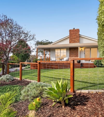 This inviting home features a spacious yard surrounded by vibrant landscaping and a welcoming front porch.