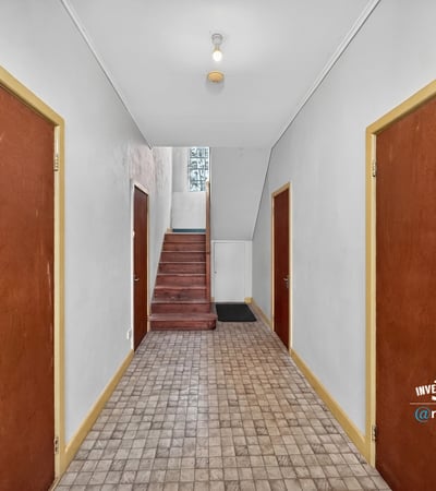Spacious hallway with wooden doors, leading to a staircase and inviting natural light throughout the space.