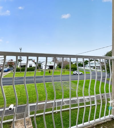 Enjoy a peaceful balcony view overlooking a quiet street surrounded by greenery and residential homes.