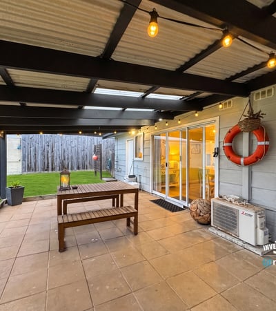 Spacious outdoor patio with hanging lights and lawn, perfect for gatherings and relaxed evenings.