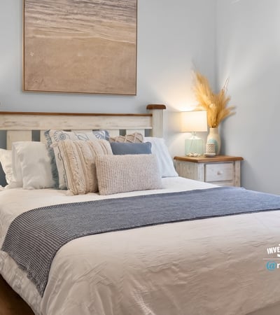 Bright and inviting bedroom features coastal decor, cozy bedding, and natural light streaming through the window.