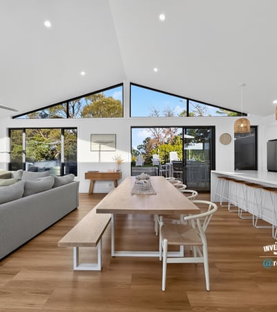 Bright and open living space seamlessly connects dining and kitchen areas, featuring large windows with natural light.