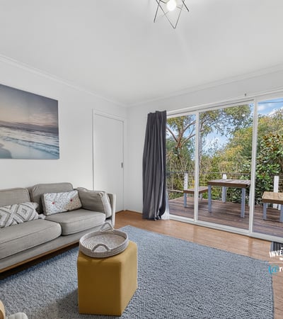 Bright living area featuring large sliding doors that open to a private outdoor deck surrounded by greenery.
