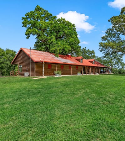 Spacious countryside home with a welcoming porch, surrounded by lush greenery and open skies.