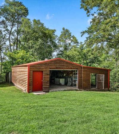 Spacious outdoor area featuring a large storage barn surrounded by lush greenery and trees.