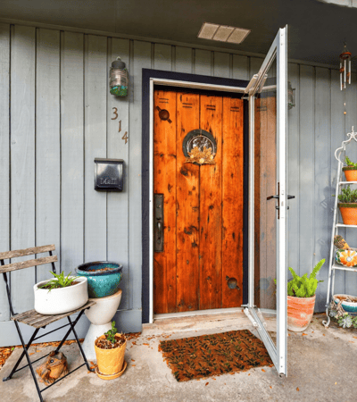 Inviting entryway featuring a striking wood door, potted plants, and a cozy seating area.