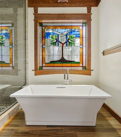 Relaxing soaking tub framed by decorative stained glass and warm wood trim. This peaceful bathroom retreat blends artistry with luxury finishes.