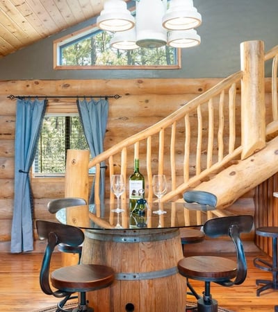 Dining area with handcrafted barrel table, log staircase, and warm wood finishes that reflect the home s authentic Prescott log construction.