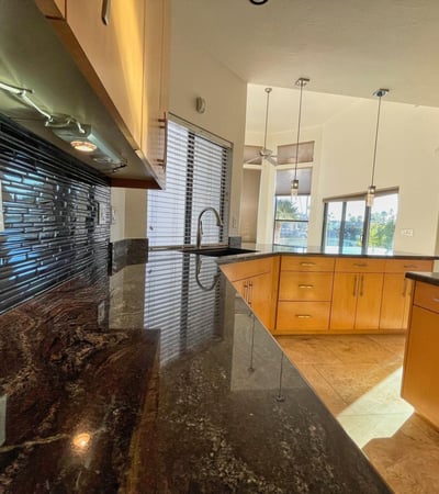 Modern kitchen showcasing high-end granite, black tile backsplash, and warm wood cabinetry for a sleek, timeless finish.