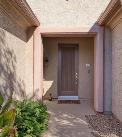 A covered entry framed by natural desert tones offers a warm welcome. Thoughtfully designed for shade and comfort, this entrance sets the tone for a peaceful home experience.