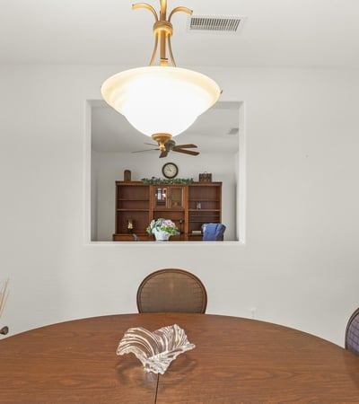 A modern dining area framed by crisp white walls and elegant lighting, offering a clear view into the private home office beyond.