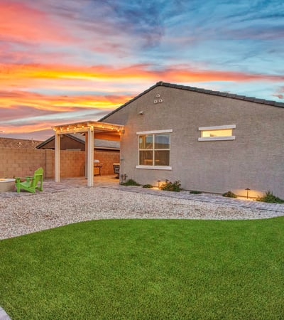 A twilight view showcases the home s well-planned backyard, featuring artificial turf, paver walkways, and accent lighting designed for beauty and efficiency in Litchfield Park.
