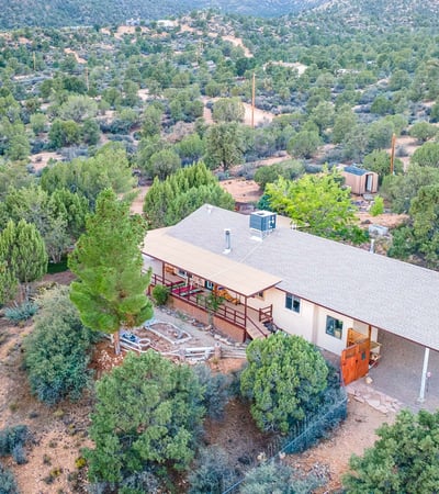 This elevated view highlights the wraparound deck, mature trees, and sprawling land. A serene retreat with endless possibilities for customization or self-sufficient living.