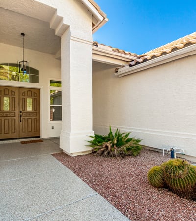 Inviting covered entry with double front doors, architectural details, and desert landscaping accents. The shaded Scottsdale entrance creates a warm and stylish arrival experience for guests and homeowners.
