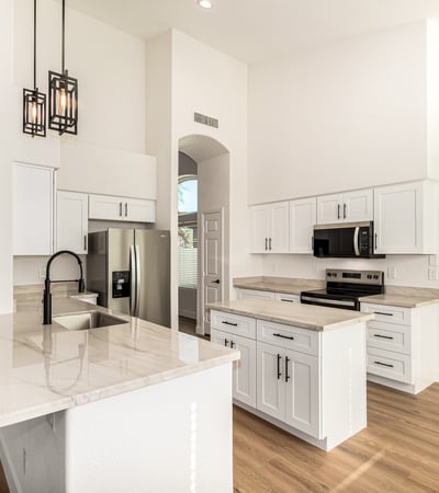 Updated Scottsdale kitchen featuring a spacious island, sleek quartz-style counters, white cabinetry, and stainless steel appliances. Modern pendant lighting and vaulted ceilings enhance the contemporary open layout.