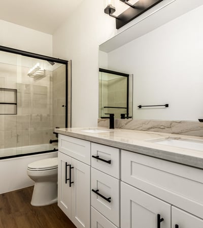 Updated Scottsdale guest bathroom with dual sinks, contemporary cabinetry, and modern black fixtures. The bathroom also includes a glass shower enclosure and elegant finishes that complement the home s remodeled interior.