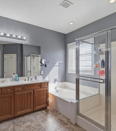 Primary bathroom with dual sinks, wood cabinetry, and bright lighting, providing a functional and stylish space for daily routines.