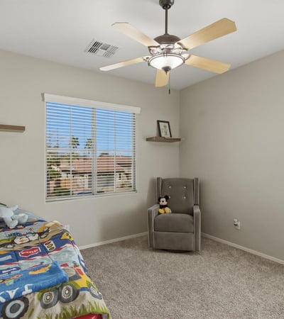 Bright bedroom with plush carpet, ceiling fan, and large window providing a welcoming space for family or guests.