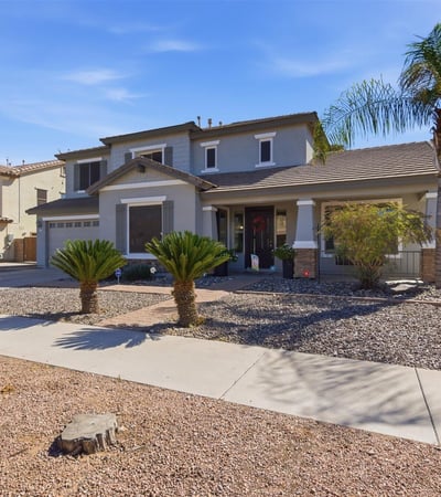 Inviting Queen Creek home exterior featuring desert landscaping, palm trees, stone accents, and a covered entry creating beautiful curb appeal.