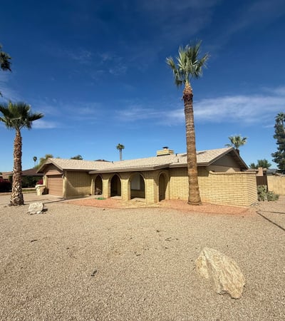 Front yard view showing wide desert landscaping and tall palm trees surrounding this Glendale home. The low-maintenance yard design complements the classic Southwestern architecture.