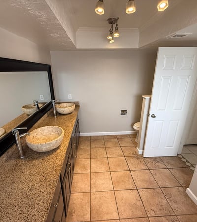 Bathroom featuring dual vessel sinks, long vanity counter, and large mirror. The design provides functionality and style within the primary suite.