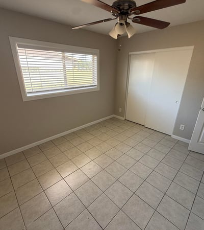 Light-filled bedroom featuring tile flooring, neutral walls, and ceiling fan lighting. The open layout makes the space perfect for guests, family members, or a home office.