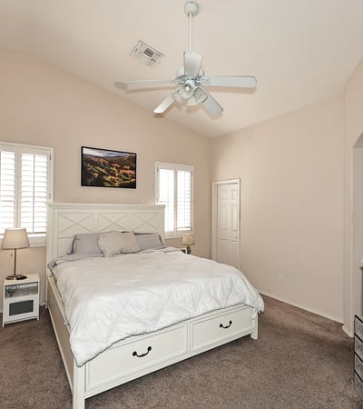 Primary bedroom with vaulted ceilings, ceiling fan, and plantation shutters. This Phoenix home offers a bright and airy space with neutral tones and plush carpet.