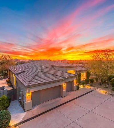 Beautifully maintained Scottsdale home with modern architecture, spacious driveway, and warm exterior lighting set against a vibrant sunset backdrop.