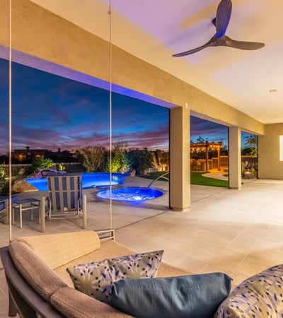 Covered patio with a modern swing seat overlooking the pool and spa, creating a unique Scottsdale outdoor living experience at night.