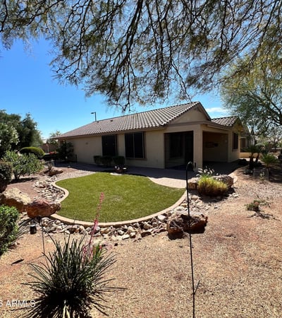 Beautiful backyard showcasing lush artificial turf, paver pathways, decorative rock features, mature desert plants, and tranquil golf course surroundings. A perfect outdoor retreat for relaxing or entertaining guests.