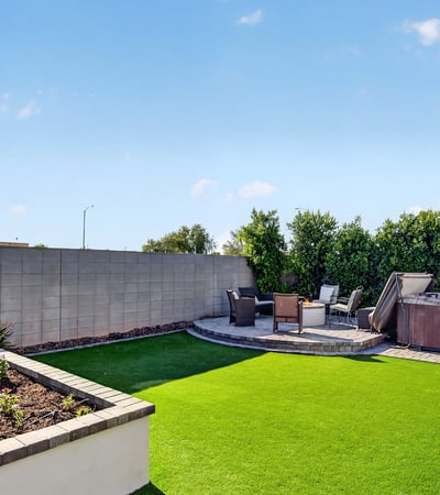 Beautiful backyard featuring artificial turf, raised garden planters, paver hardscaping, and a private hot tub creates a low-maintenance outdoor oasis in Surprise.