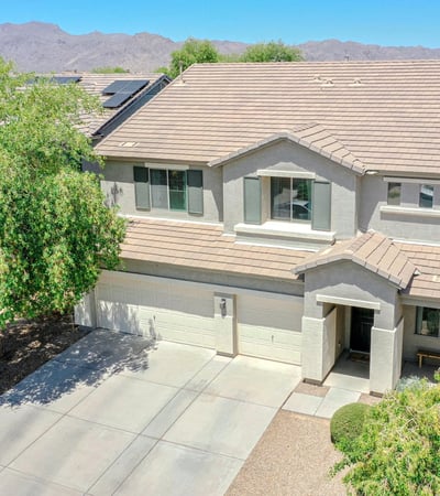 Elevated drone view highlighting the home's impressive exterior, expansive driveway, mature trees, and scenic mountain backdrop. A beautiful overview of this exceptional Waddell proper