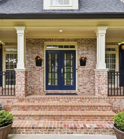 Welcoming entrance features a brick facade, dual blue doors, and attractive landscaping for a polished look.