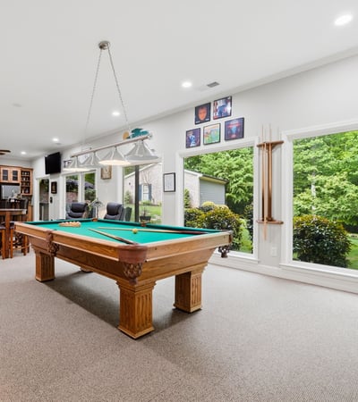 Spacious recreational room featuring a billiard table, large windows, and scenic views of the landscaped yard.
