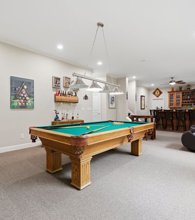 Spacious recreational room featuring a pool table and a well-equipped bar, perfect for entertaining.