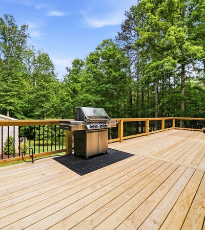 Spacious outdoor deck featuring a built-in grill, perfect for gatherings amidst lush greenery.