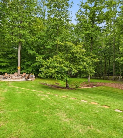Spacious backyard with a cozy fire pit surrounded by lush greenery, perfect for gatherings and relaxation.