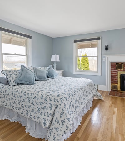 This inviting bedroom features large windows, cozy furnishings, and a warm brick fireplace, perfect for relaxation.
