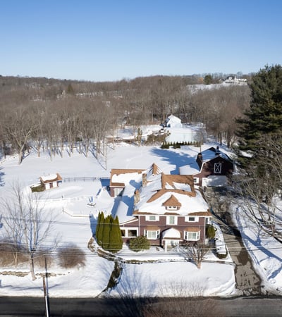 This expansive property features a beautiful home surrounded by lush trees and serene winter landscapes.