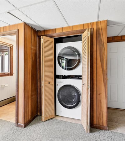 Convenient laundry area with stacked washer and dryer, featuring warm wood paneling and easy access.