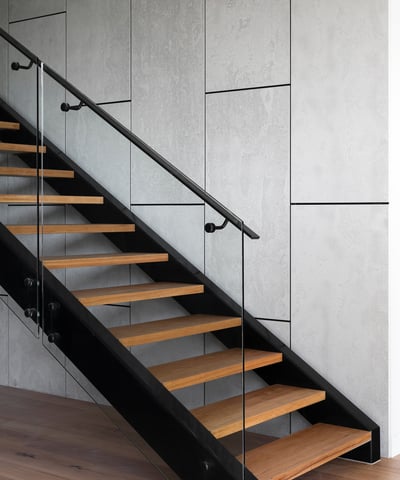 Modern staircase featuring sleek glass railing and warm wooden steps against a stylish gray backdrop.