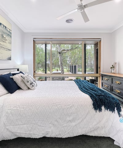 Spacious bedroom featuring large windows, natural light, and a view of lush outdoor greenery.
