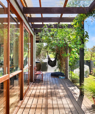 This inviting covered deck offers a perfect blend of indoor-outdoor living, surrounded by lush greenery.