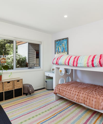 Bright and inviting bedroom featuring bunk beds, ample storage, and a large window overlooking the garden.