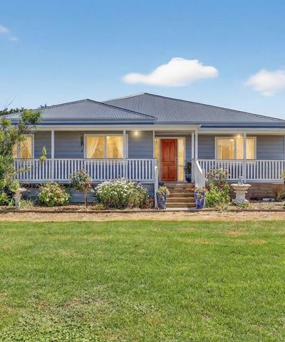 Spacious home surrounded by landscaped gardens, featuring a welcoming porch and ample outdoor space for relaxation.