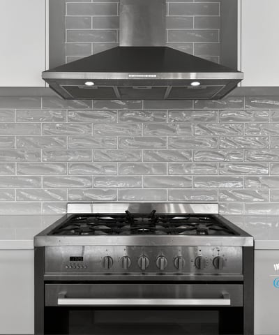 Modern kitchen featuring a stainless steel gas range and sleek gray tile backsplash for optimal cooking experience.