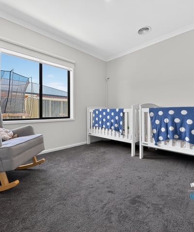 Bright nursery featuring twin cribs, a cozy rocking chair, and large windows for ample natural light.