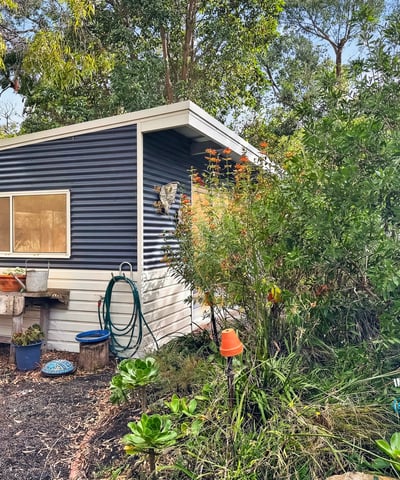 Quaint cottage nestled among lush greenery, offering a unique retreat with potential for creative landscaping.