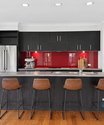 Modern kitchen featuring sleek cabinetry, a striking red backsplash, and spacious island with bar seating.