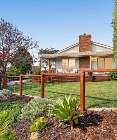 This inviting home features a spacious yard surrounded by vibrant landscaping and a welcoming front porch.